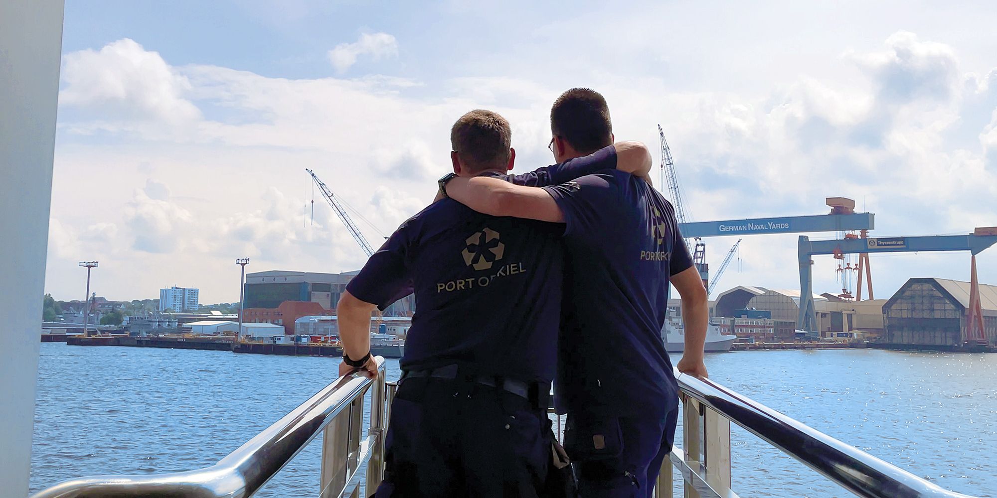 Zwei Mitarbeiter*innen blicken auf den Kieler Hafen